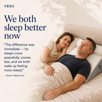 A couple sleeping peacefully in bed with a white comforter and a beige headboard. A woman rests on the man's shoulder, smiling at the camera.